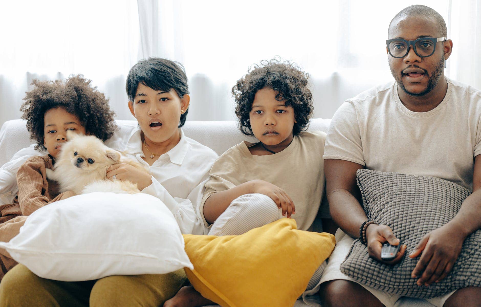 interested multiracial family watching tv on sofa together with dog