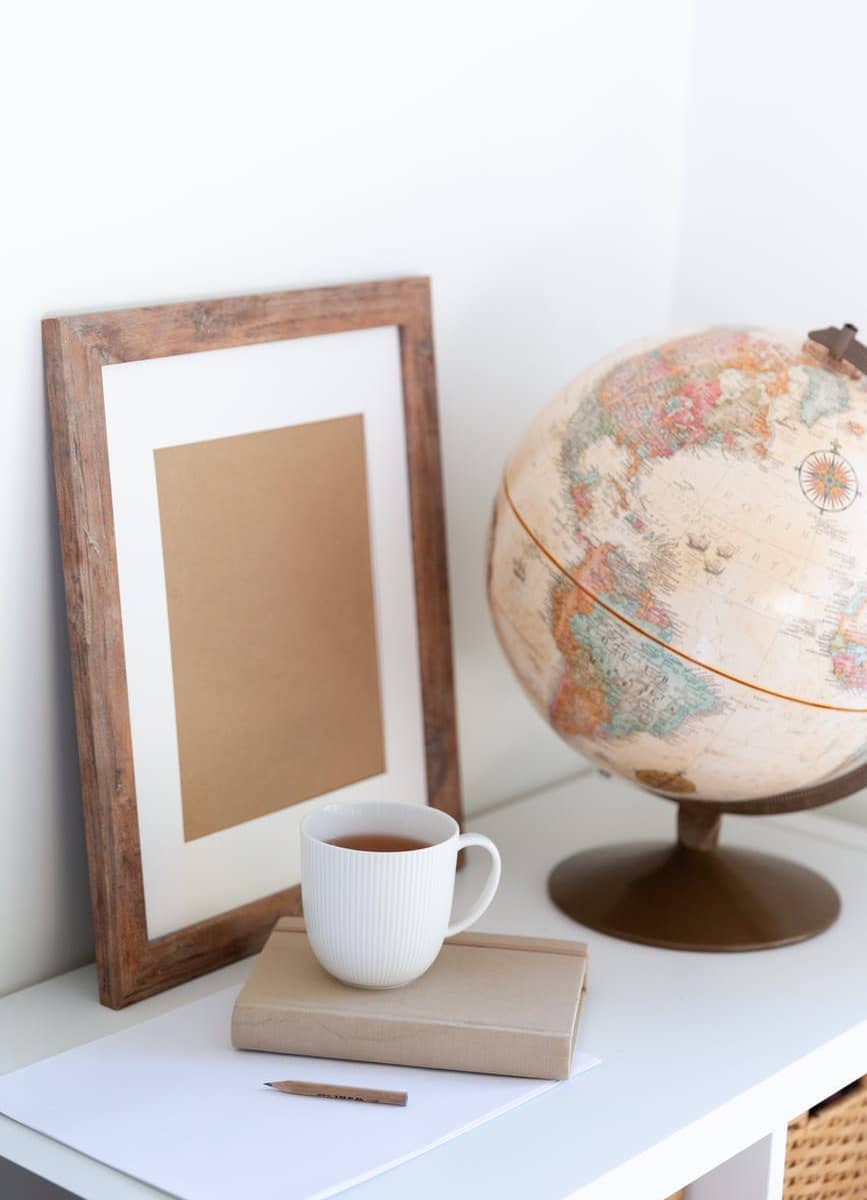 vintage globe near blank frame and cup of tea placed on book in office