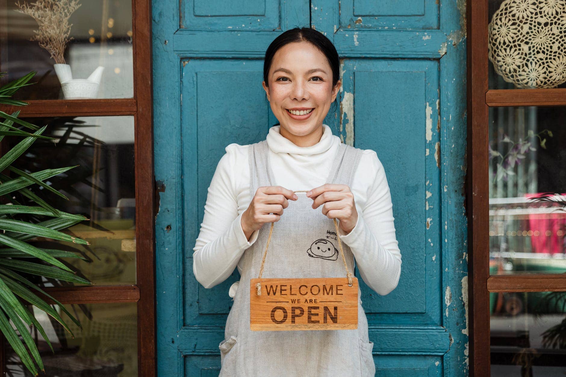 Simple Life Style 1: Apron-ed shop owner holding a welcome we are open sign.  Photo by Ketut Subiyanto on Pexels.com
