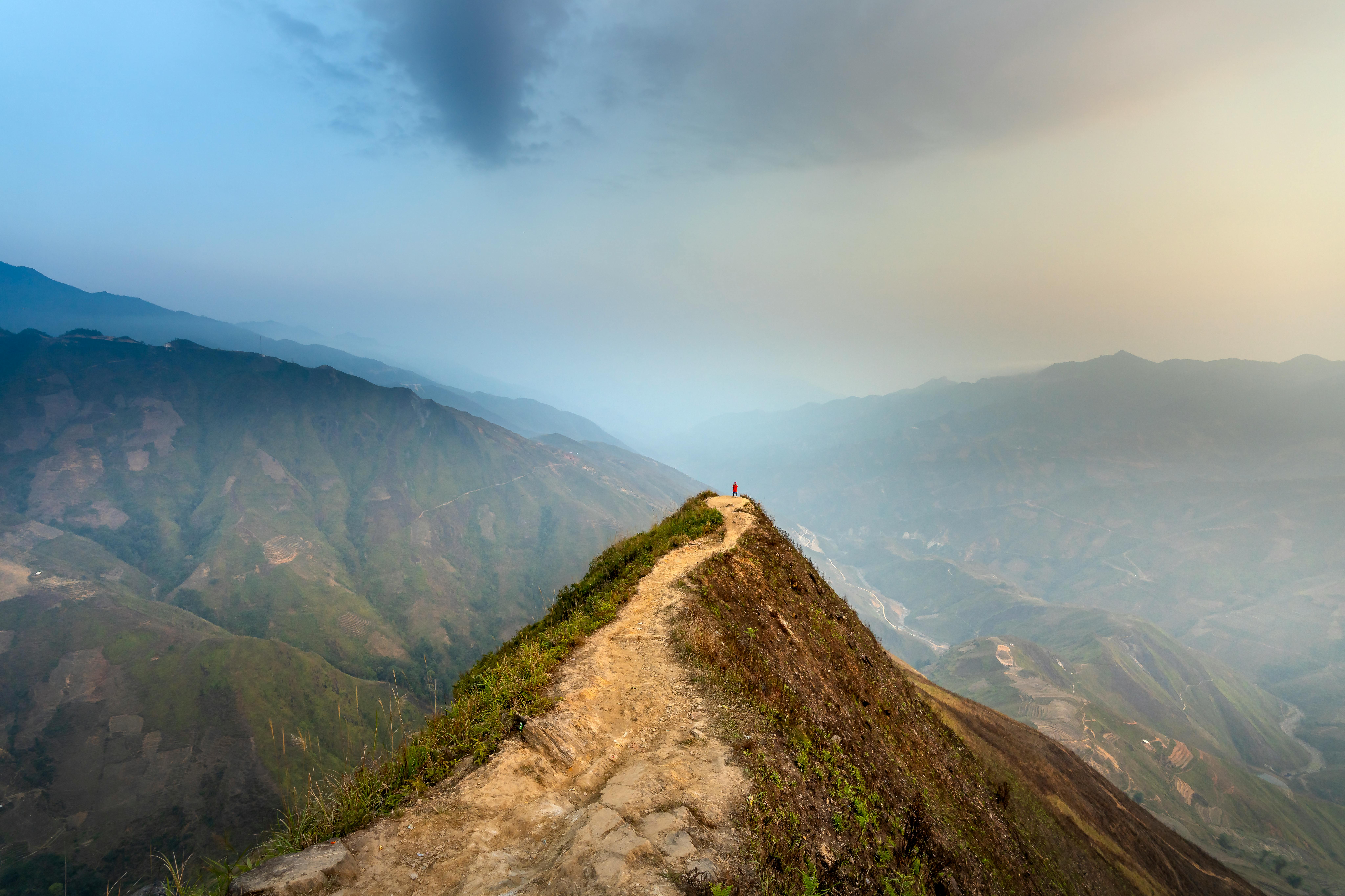 Narrow footpath leading to edge of amazing mountain cliff with traveler standing on top observing picturesque terrain