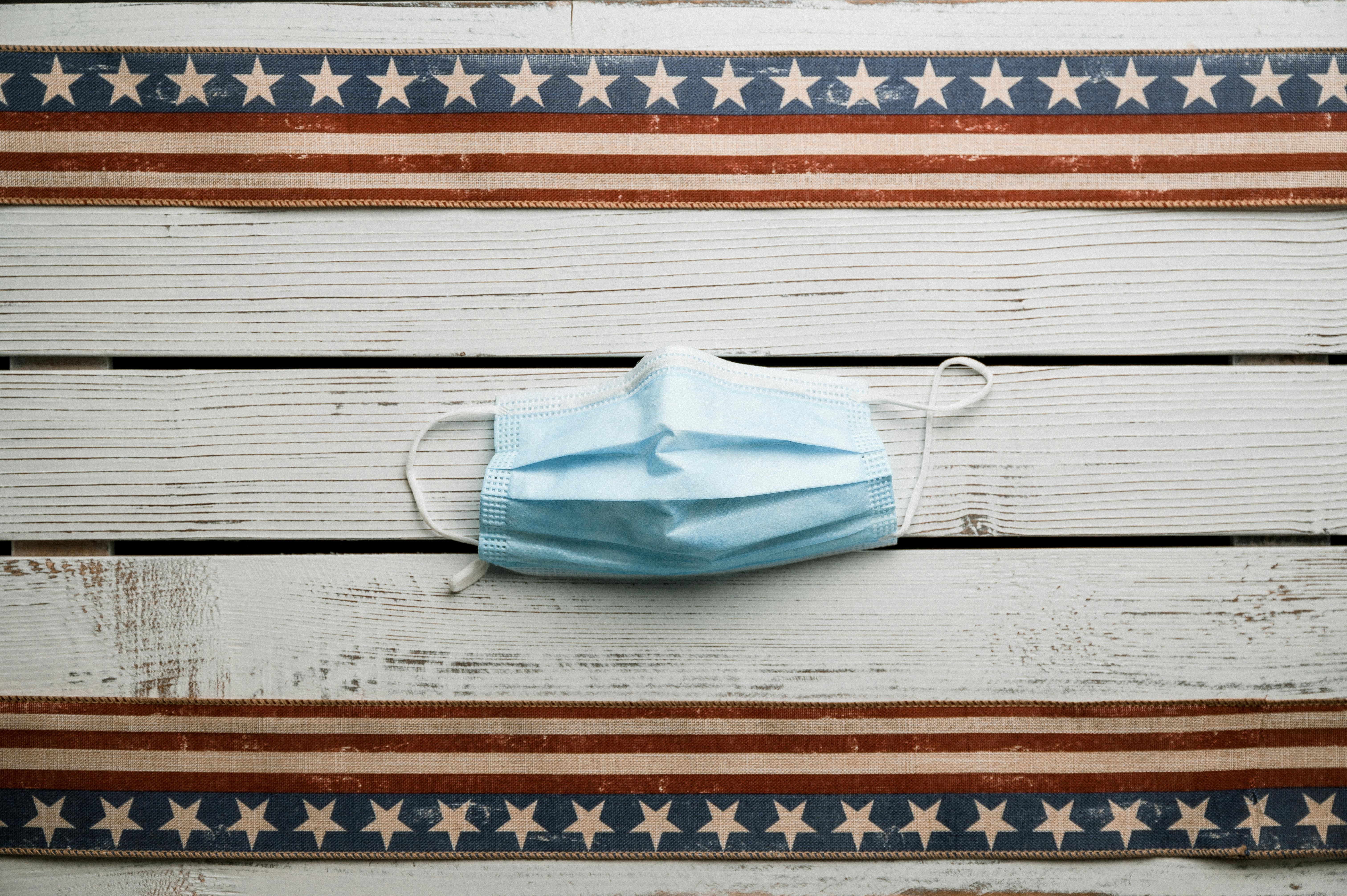 Top view of sterile face mask placed on white shabby wooden table with American flag ribbons